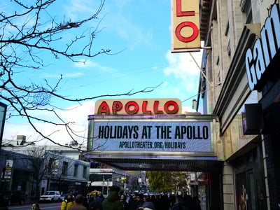 The sign of the Apollo Theater in Harlem announcing events for the holidays, surrounded by an enthusiastic crowd.
