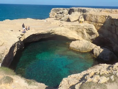 A turquoise water basin surrounded by cliffs overlooking the ocean, located at the Caves of Poetry.