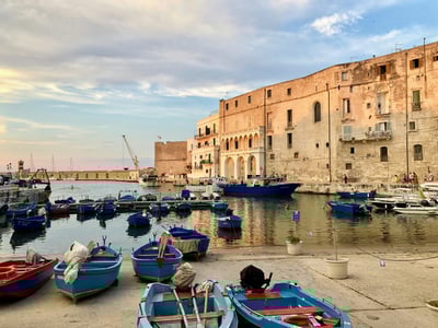 Bateaux colorés au port de Monopoli, face à des bâtiments historiques sous un ciel nuageux au crépuscule.