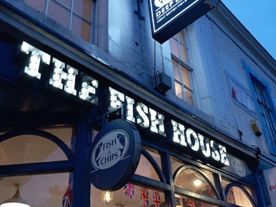 The entrance of the Fish House, lit at dusk, showcasing fish and chips dishes in a bustling street.