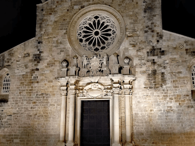 Illuminated facade of the Cathedral of Saint Mary Annunziata, highlighting the rose window and the detailed sculptures.