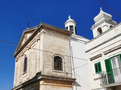 Facade of the Santuario di San Rocco in Alberobello, highlighting its unique architecture under a bright blue sky.
