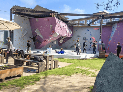 Outdoor climbing area at Bright Site, with climbers on the colorful wall and a wooden rest area.
