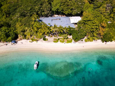 Quiet beach in Cairns, with a hut surrounded by palm trees and a fishing boat in the crystal-clear waters.