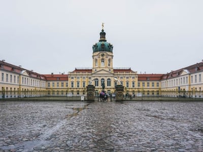 Impressive facade of the Charlottenburg Palace, with its green dome and gardens, under a cloudy sky.