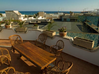 Vue panoramique depuis la terrasse de la Villa Bruno, avec des meubles en bois et la mer au loin. Un lieu idéal pour se détendre.