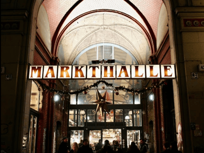 Illuminated entrance of the Markthalle Neun in Berlin, with visitors and festive decorations.