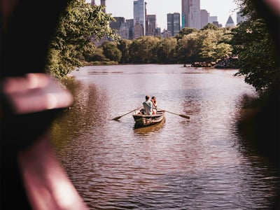 Bateau traditionnel avec un couple pagayant tranquillement dans le lac de Central Park, entouré de la skyline de New York.