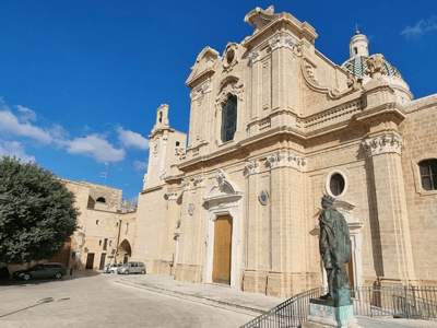Elegant facade of the church near the Porta degli Ebrei in Malta, with a bronze statue in the foreground.