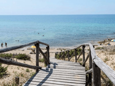 Access to the beach of Campomarino di Maruggio, with turquoise sea and bathers enjoying the sun on the sand.