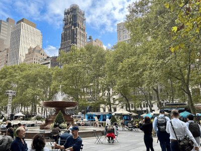 Fountain in the center of Bryant Park, surrounded by greenery and visitors enjoying the urban buzz and the blue sky.