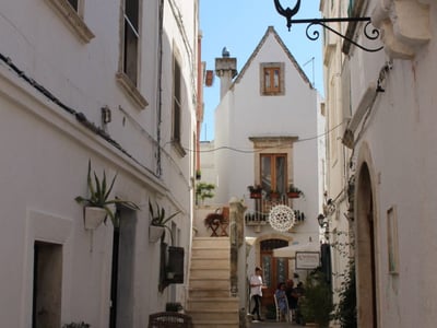 Rue pittoresque de Cisternino, avec des maisons blanches et des escaliers menant à un café animé.