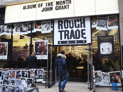 Entrée de Rough Trade East, mettant en avant l'album du mois de John Grant, entourée de passionnés de musique.