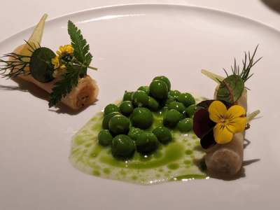 Assiette élégante de petits pois, crème verte et fleurs comestibles, mettant en valeur la cuisine innovante de Cookies Cream.