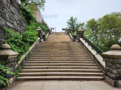 Stone steps leading to Morningside Park, surrounded by greenery, under a cloudy sky. Perfect for a peaceful stroll.