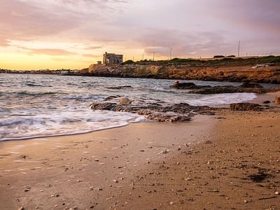 Torre Ovo beach at sunset, where the waves caress the sand and an ancient building overlooks the sea.