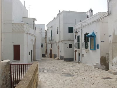 Narrow alley in Castellaneta, with white walls and colorful windows, evoking Mediterranean charm.