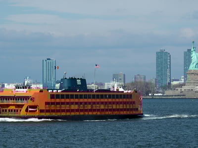 Orange Staten Island ferry navigating in the bay with skyscrapers in the background, a symbol of New York City.