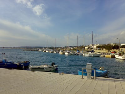 View of the port of Torre Vado with moored boats and a partially cloudy sky, perfect for a day at sea.