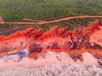 Vibrant landscape of Broome, revealing spectacular red formations by the sea, surrounded by lush greenery.