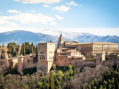 Vue panoramique de l'Alhambra à Grenade, avec la Sierra Nevada en arrière-plan, illustrant l'architecture mauresque.