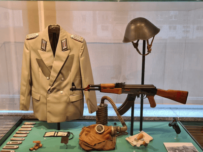 Uniforme ancien de la Stasi avec un fusil, un casque, et des accessoires historiques exposés au Musée de la Stasi à Berlin.