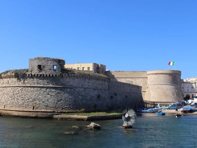 Historical fortifications at the Port of Gallipoli, with a view of the water and typical boats in the background.