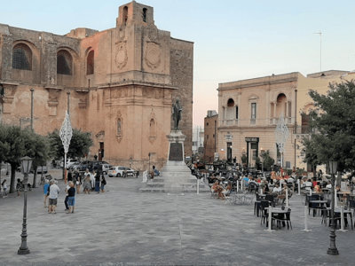 Lively square in Tricase, with a central statue, terrace cafés, and historic buildings in the background.