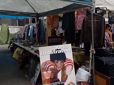 Flea market stand in Chelsea, featuring vintage clothing and a prominently displayed Sports Illustrated magazine.