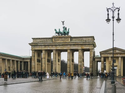 The Brandenburg Gate, a symbol of Berlin, attracts visitors under a gray sky, framed by historic monuments.