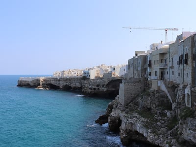 Côte rocheuse de Grotta Piana avec des bâtiments en bord de mer et une vue sur l'eau turquoise sous un ciel dégagé.