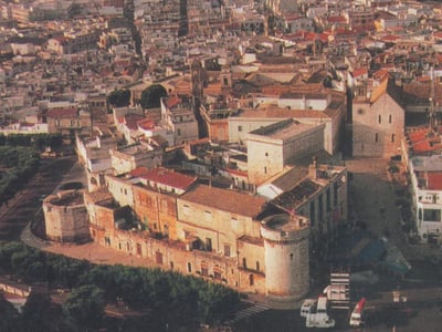Vue aérienne du Château San Benedetto, entouré de maisons historiques et de rues animées, illustrant le patrimoine de la région.