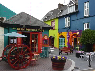 Café vivant à Kinsale avec façades colorées et plantes fleuries, montrant l'animation locale du marché.