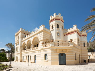 Villa Raffaella, an elegant villa with Mediterranean architecture, surrounded by palm trees and a clear blue sky.