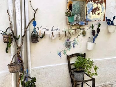 Mur décoré avec des pots de fleurs, des accessoires en osier et un cadre vintage, capturant l'âme artistique de Locorotondo.