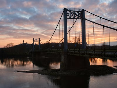 Le pont suspendu de Préban au coucher du soleil, reflétant la beauté paisible de la rivière et de la nature environnante.