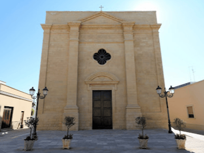 Façade imposante d'une église à Acaya, avec un portail en bois central et des lanternes élégantes de chaque côté.