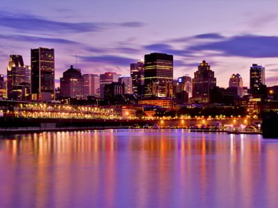 Panoramic view of the Montreal skyline at dusk, illuminated by the lights of the buildings and reflected in the water.