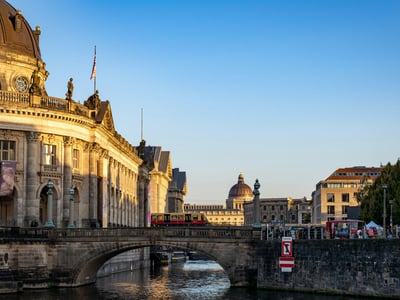 Vue de la Museumsinsel avec un tram circulant sur un pont, illuminée par la lumière dorée du coucher de soleil.