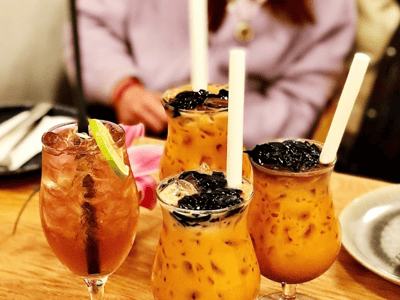 Quatre cocktails colorés servis sur une table en bois à Larb Koi, mettant en valeur la convivialité du restaurant.