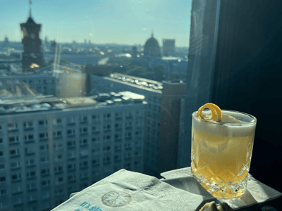 Panoramic view of Berlin from the Rooftop One Alexanderplatz, with a cocktail and snacks on a luminous table.