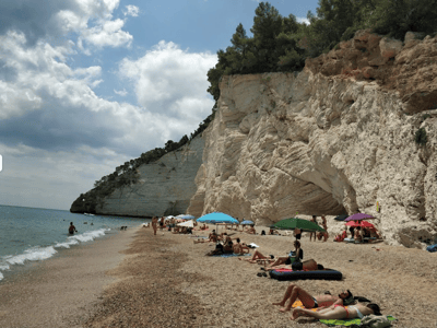 Lively beach of Vignanotica Bay, with colorful umbrellas, white cliffs, and bathers enjoying the sun.