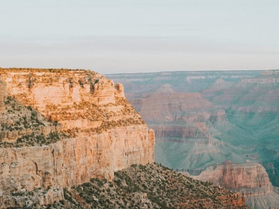 Vaste panorama du Grand Canyon avec falaises majestueuses et vallée verdoyante, capturant la beauté naturelle incomparable du site.