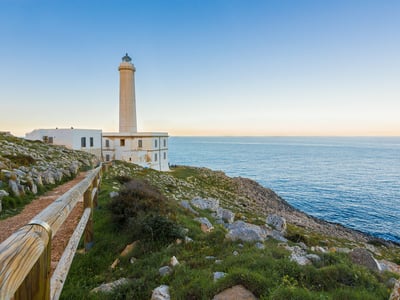 Majestic lighthouse overlooking the sea, surrounded by lush landscapes in Costa Otranto National Park.