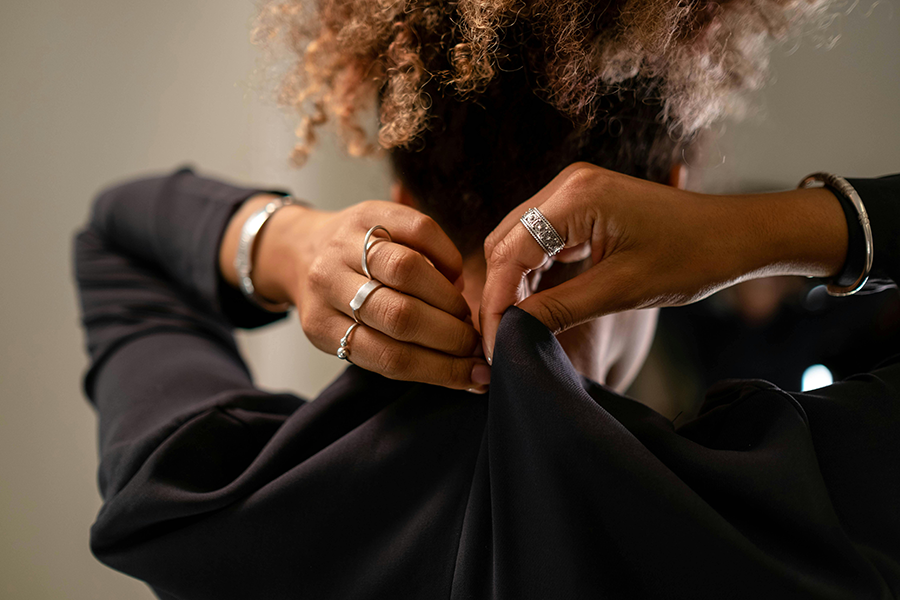 Get dressed and ready for work A person with curly hair fastens the back of a black top, wearing multiple rings and a bracelet on each wrist.