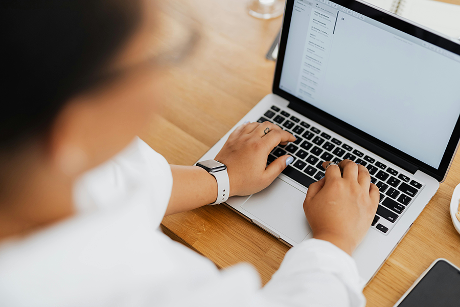Add an email signature through webmail Person wearing a smartwatch typing on a laptop at a wooden desk, with a notebook and pen visible in the background.