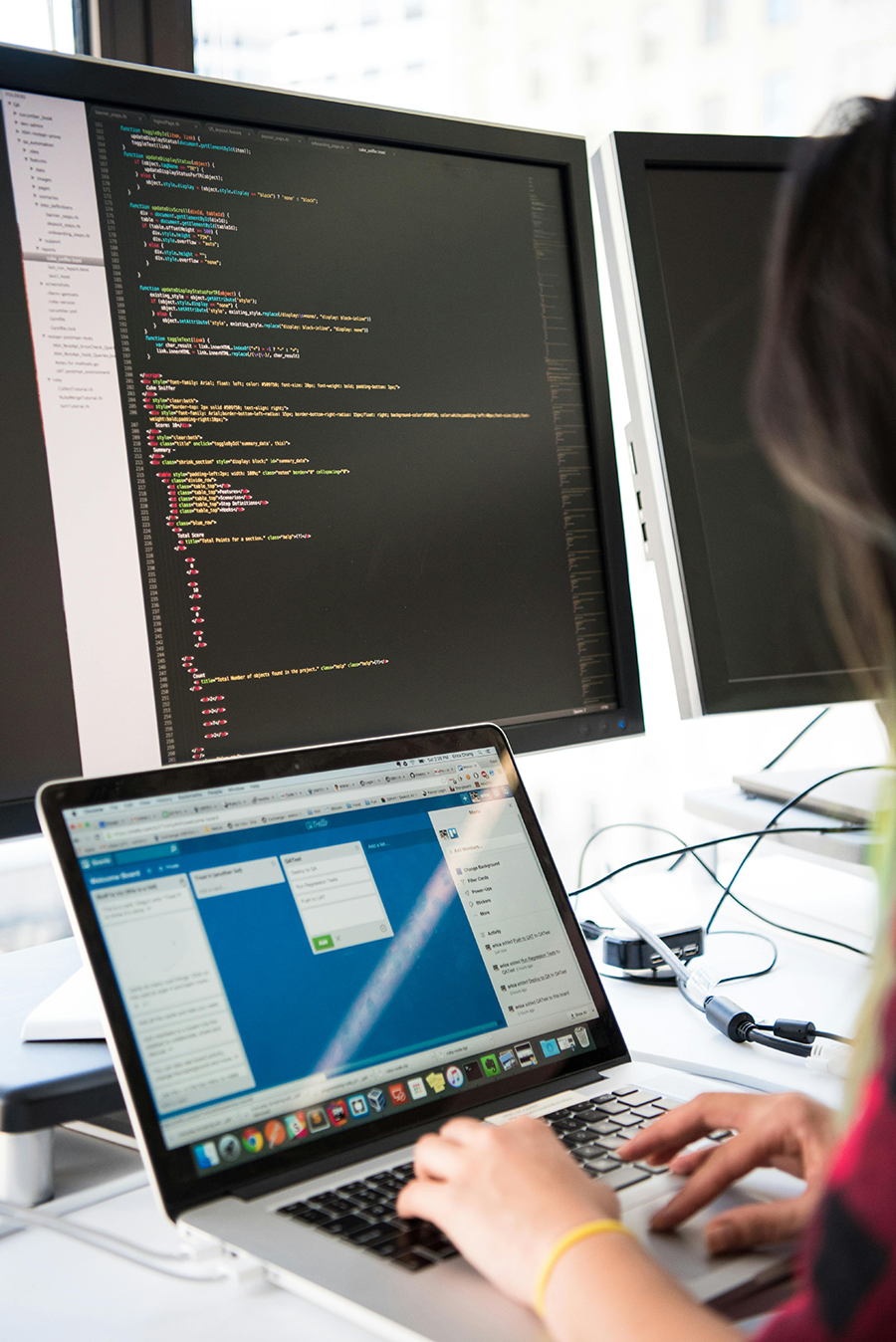 Bulk Data Upload Services Person typing on a laptop with code displayed on two large monitors in the background.