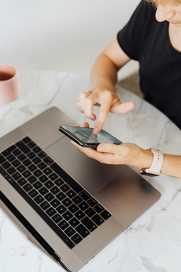 Set up email on your iPhone Person using a smartphone while sitting at a marble table with a laptop and a pink mug.