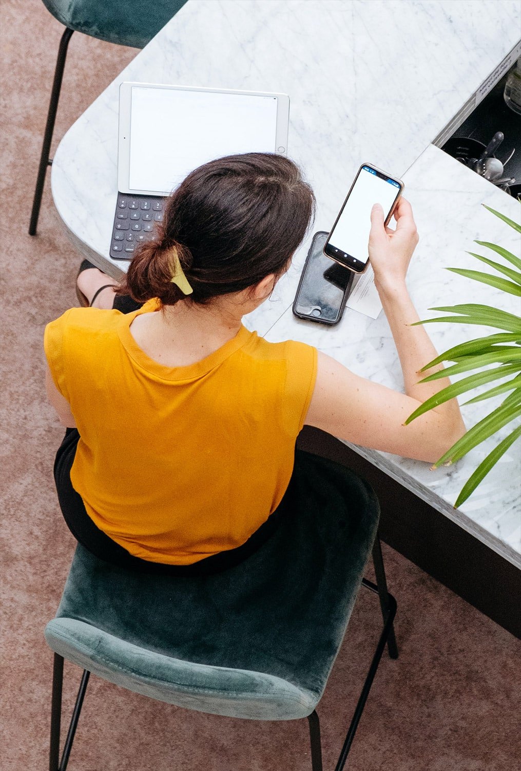 A person is using a mobile phone while seated at a table with a chair in an indoor setting.