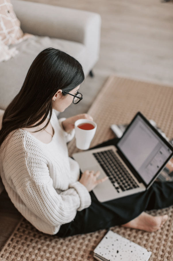 A woman sitting on the floor managing her site with a laptop and a cup of tea.